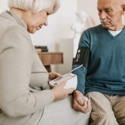 Wife helping her husband take his blood pressure with an at home monitor.